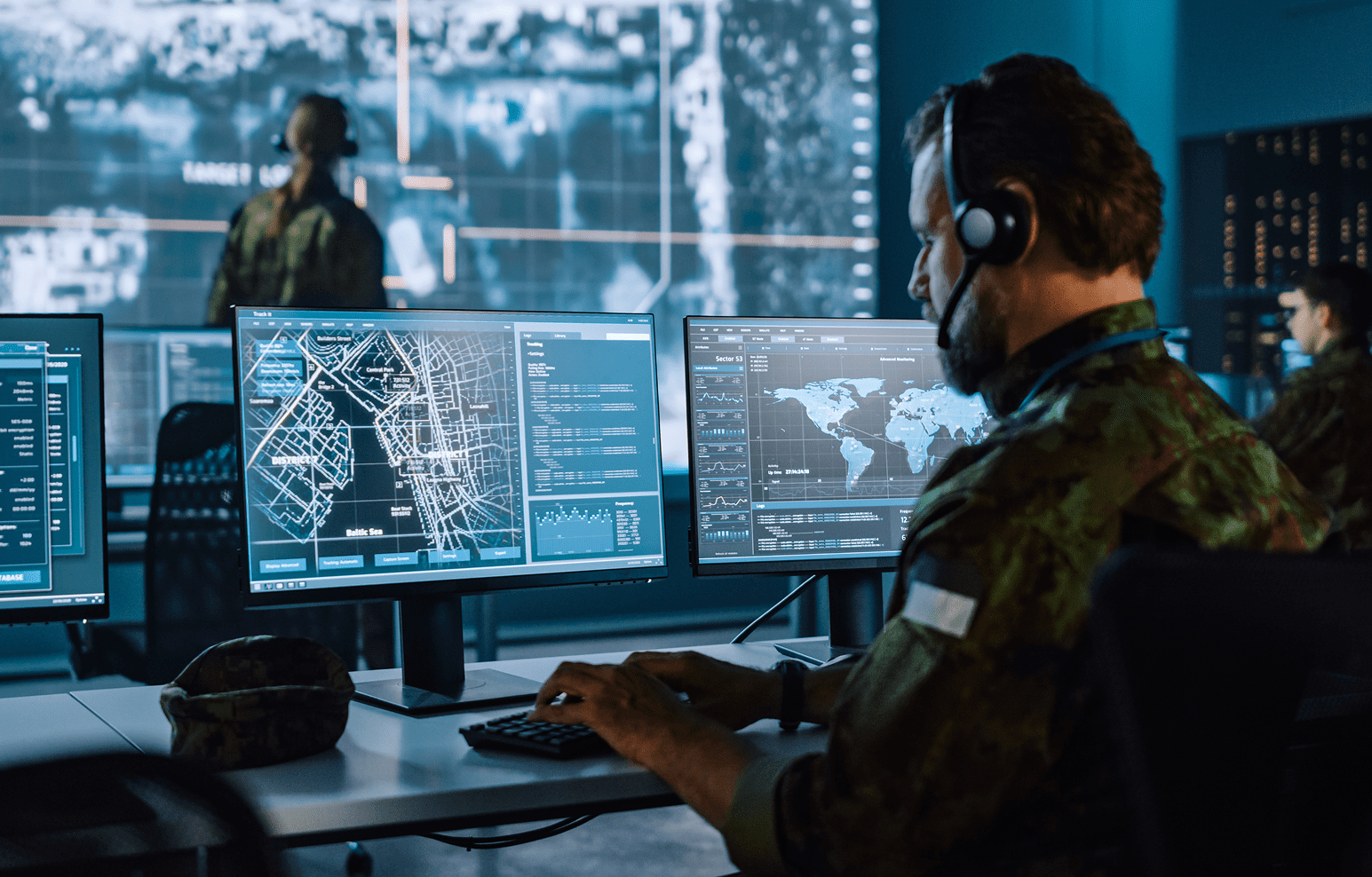 Military personnel monitoring global data on multiple computer screens.