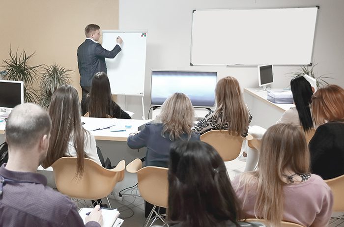 Teacher explaining concepts on a whiteboard to attentive students in a classroom.