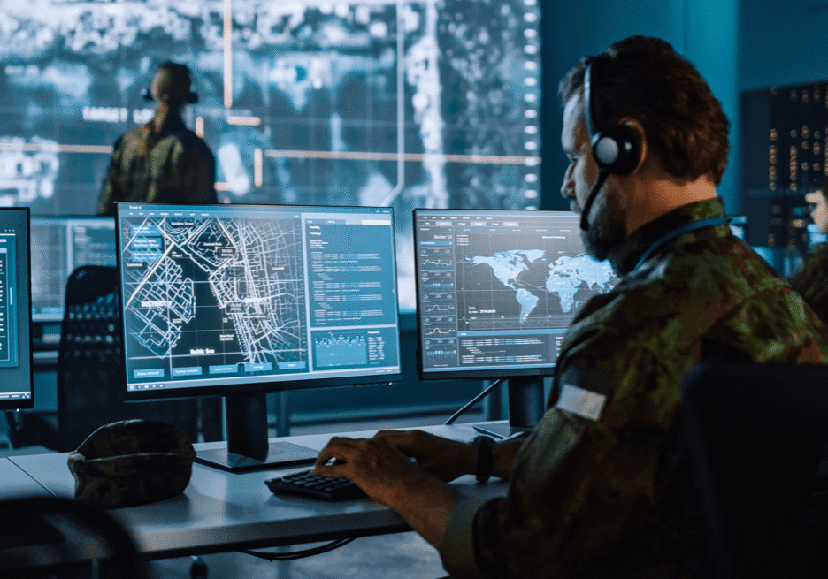 Military personnel monitoring global data on multiple computer screens.